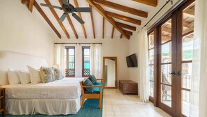 Un dormitorio con cama, una silla, televisor y un ventanal grande.