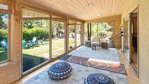 Un espace extérieur abrité, doté de grandes portes-fenêtres coulissantes, d’un plafond en bois et de tapis à motifs.