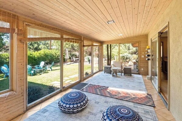A covered outdoor area with large sliding glass doors, wooden ceiling, and patterned rugs.