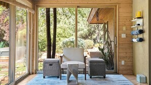 Un intérieur moderne avec une grande porte-fenêtre coulissante donnant sur un jardin, des meubles en osier et une étagère où sont rangés des objets enroulés.