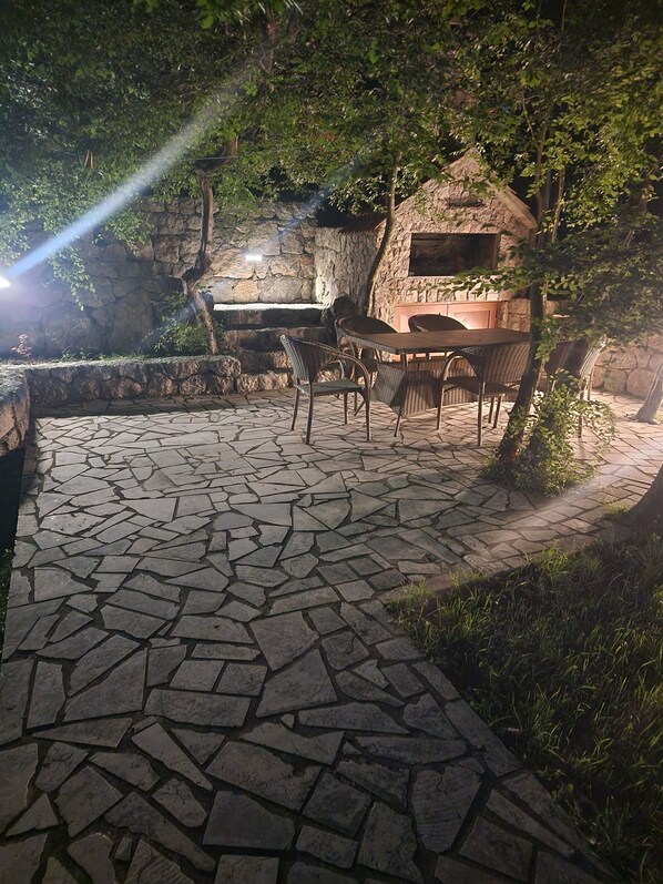 An outdoor patio with stone flooring, wicker furniture, and a stone wall backdrop. - PEACE OF HEAVEN (kotor)