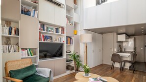 A modern living room with a green sofa, a flat-screen TV, and a dining area with a table and chairs. - Bright & Chic Duplex with A/C – Heart of Paris 9th (Paris)