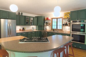 Een keuken met groene kastjes, een granieten aanrechtblad, een gasfornuis, roestvrijstalen apparatuur en een raam met uitzicht.