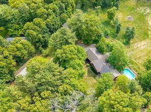 Luchtbeeld van een woonhuis met zwembad, omgeven door weelderige begroeiing en bomen.