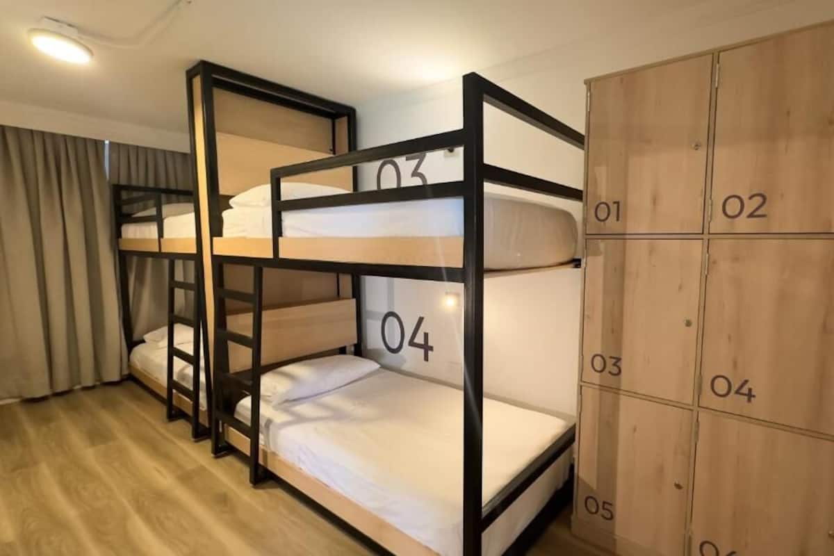 A bunk bed room with four numbered beds and a wooden wardrobe.