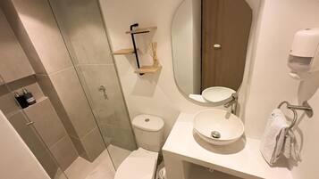 A modern bathroom with a glass shower enclosure, a toilet, a sink with a mirror, and a soap dispenser.