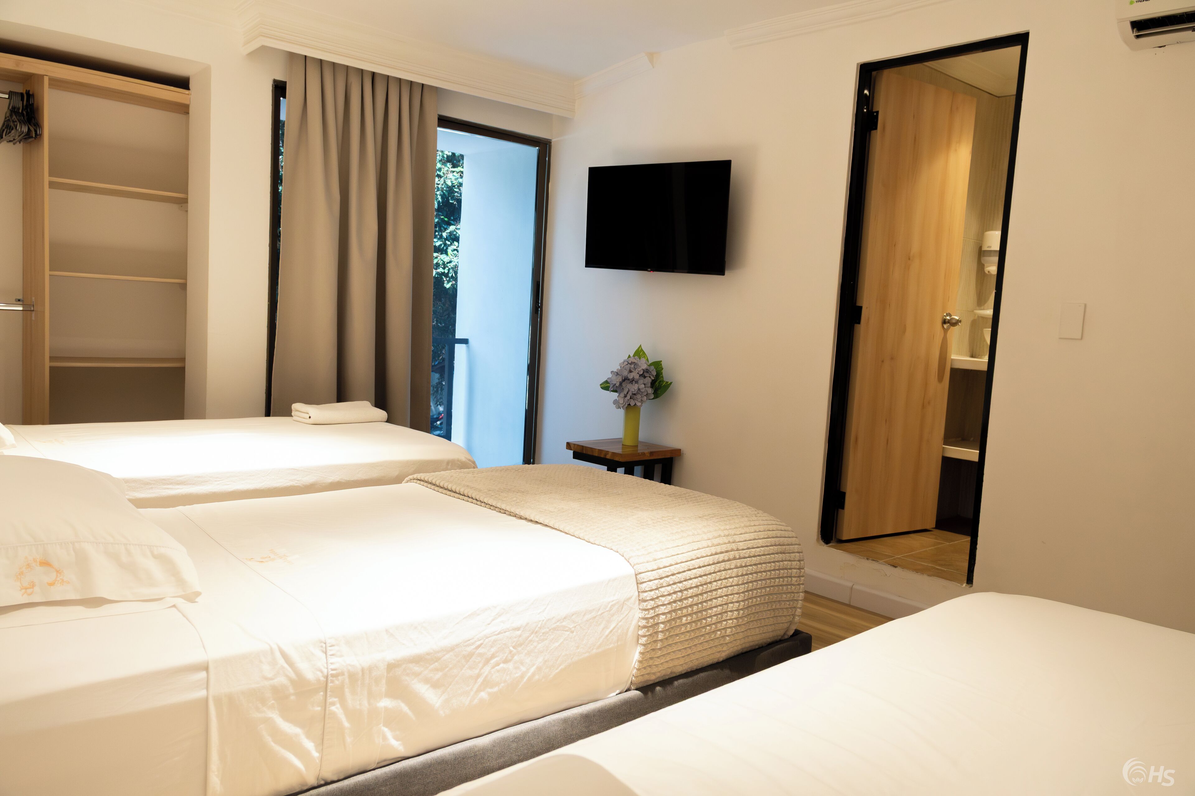 Ein Hotelzimmer mit zwei Betten, einem Fernseher, einem Kleiderschrank und einem durchgegangenes Badezimmereingang erkennbaren Bad.