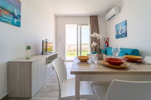 Comedor con mesa para dos, televisor y vistas al exterior.