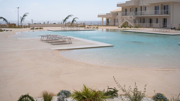 Ein Resort mit einem großen Pool, einem Gebäude mit Balkonen und ungehindertem Blick auf den Ozean.