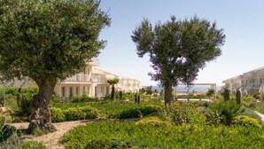 Ein Resort mit mehreren Gebäuden, einem angelegten Garten mit Bäumen und Blick auf das Meer.