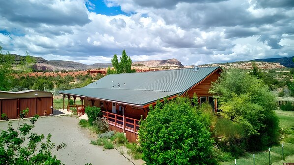 Een rustieke chalet met een metalen dak, omgeven door weelderige begroeiing en bergen op de achtergrond.