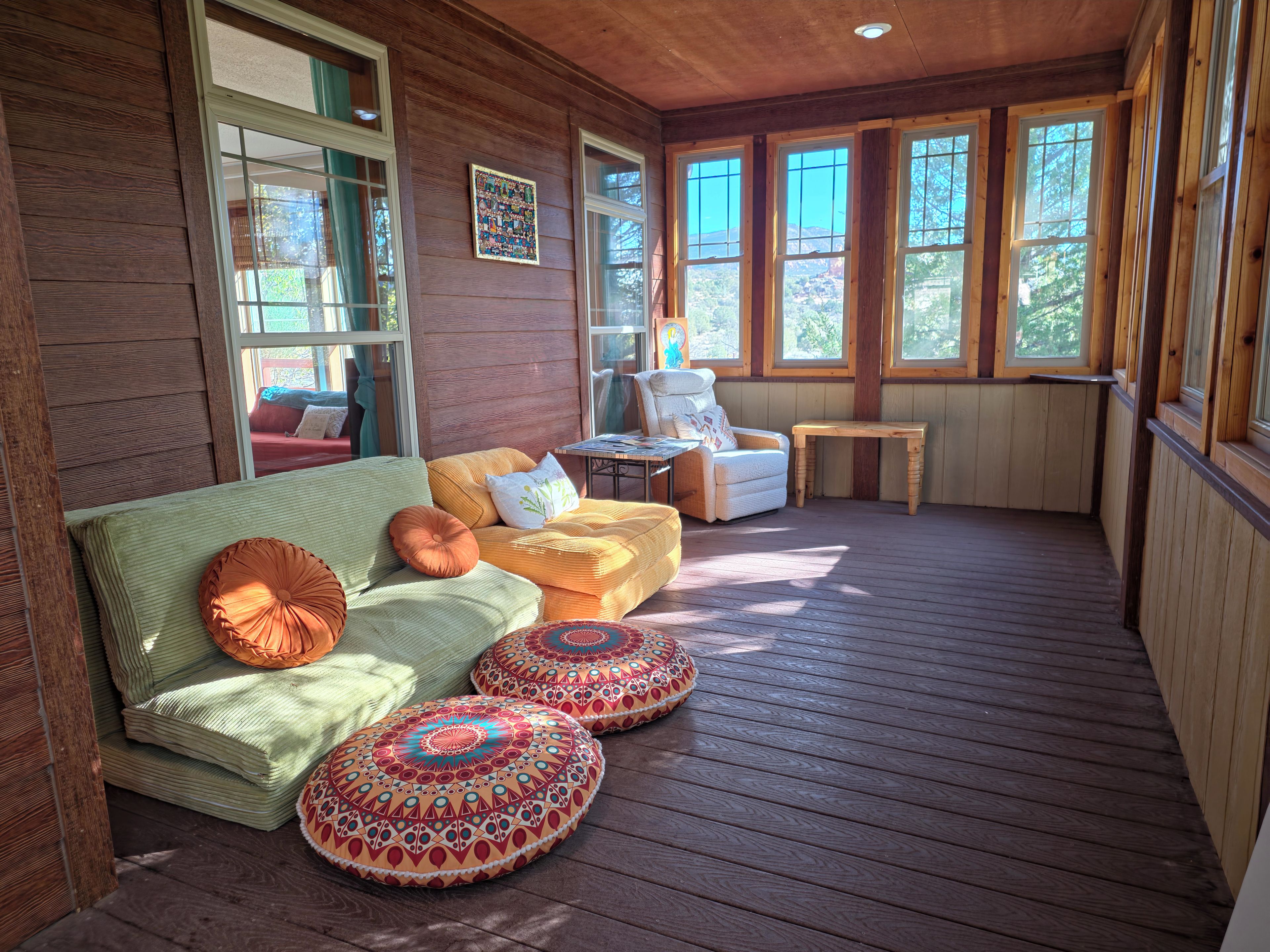 Eine Holzterrasse mit einer Couch, Poufs, einem Sessel und einem Tisch.