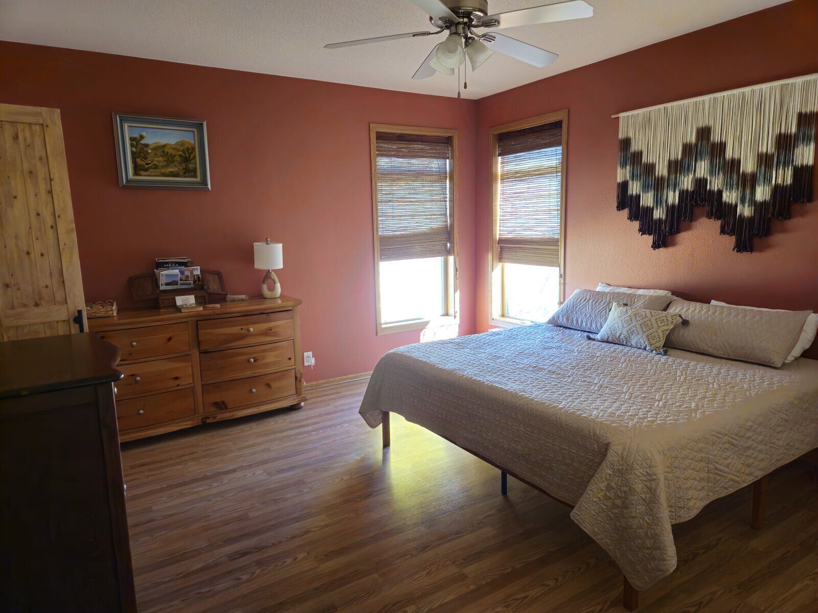 A bedroom with a bed, wooden dresser, ceiling fan, and a wall-mounted tapestry.