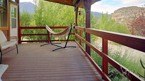 Une terrasse en bois avec un hamac et une chaise, offrant une vue sur un paysage montagneux.