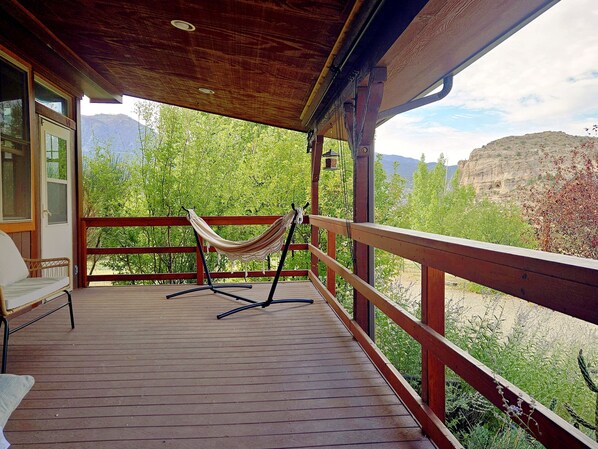 Une terrasse en bois avec un hamac et une chaise, offrant une vue sur un paysage montagneux.