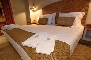 Un lit bien fait, avec des draps blancs et deux couvertures marron tissées, une tête de lit en bois et une petite table de chevet avec une lampe.