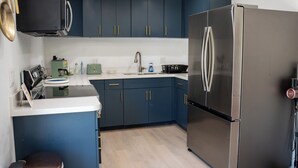Una cocina moderna con armarios azul oscuro, un refrigerador de acero inoxidable y una encimera con varios electrodomésticos.
