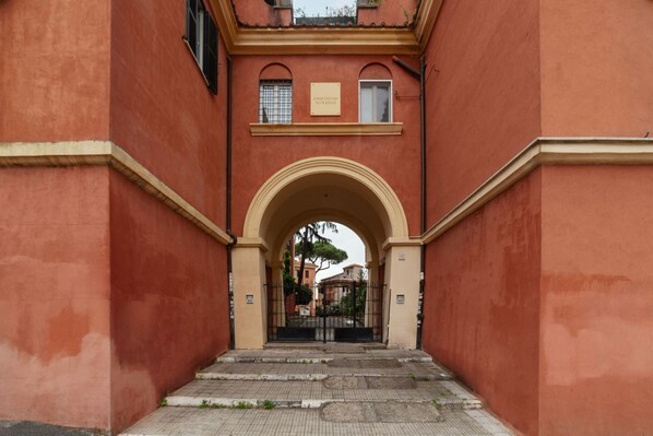 A red building with an arched entrance, a plaque, and a gated area.