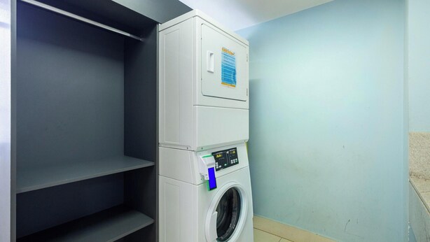 A laundry room with a stacked washer and dryer, a control panel, and a blue wall. - Metropolitan Sidney - MSS (Goiânia)