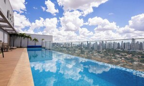 A rooftop pool with a cityscape view, palm trees, and outdoor seating. - Metropolitan Sidney - MSS (Goiânia)
