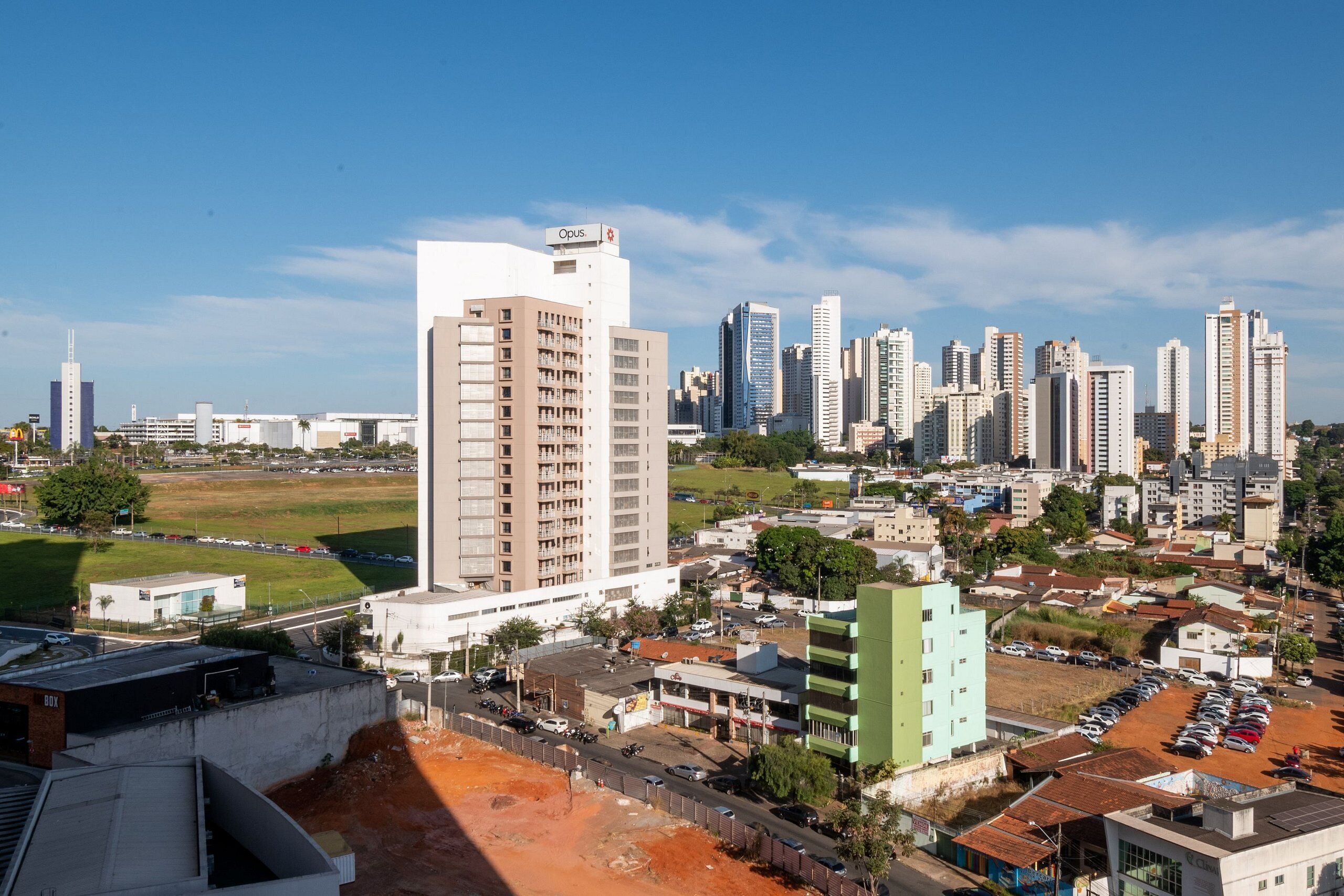 A cityscape with high-rise buildings, a parking lot, and a green field.
