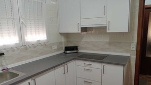 A kitchen with white cabinets, a grey countertop, a toaster, and a window with lace curtains.