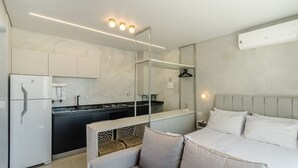 Une chambre d’hôtel moderne dotée d’une kitchenette, d’un lit avec du linge de lit blanc et d’un grand miroir.