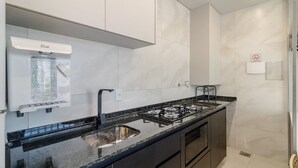 Une cuisine moderne équipée d’une cuisinière à gaz, d’un évier en acier inoxydable et de meubles blancs.