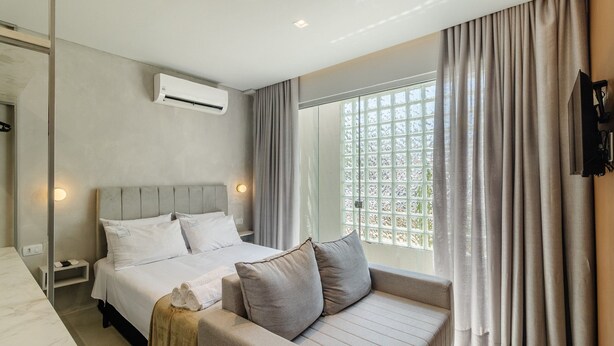 Une chambre d’hôtel moderne équipée d’un lit, d ’un canapé, d’un appareil de climatisation et d’une fenêtre avec des rideaux.