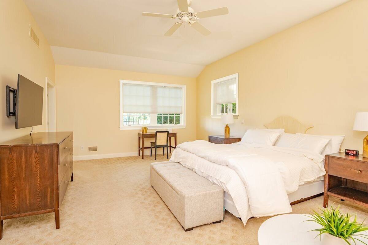 Une chambre à coucher comprenant un lit, une table de chevet, une commode, un bureau, une chaise et un téléviseur fixé au mur.