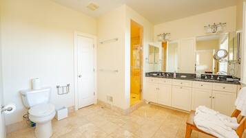 A bathroom with a toilet, bidet, shower, vanity with a mirror, and a towel rack.