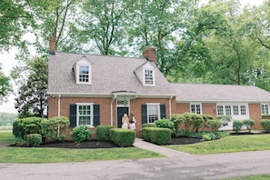 A brick house with a front porch, a chimney, and a well-maintained lawn.