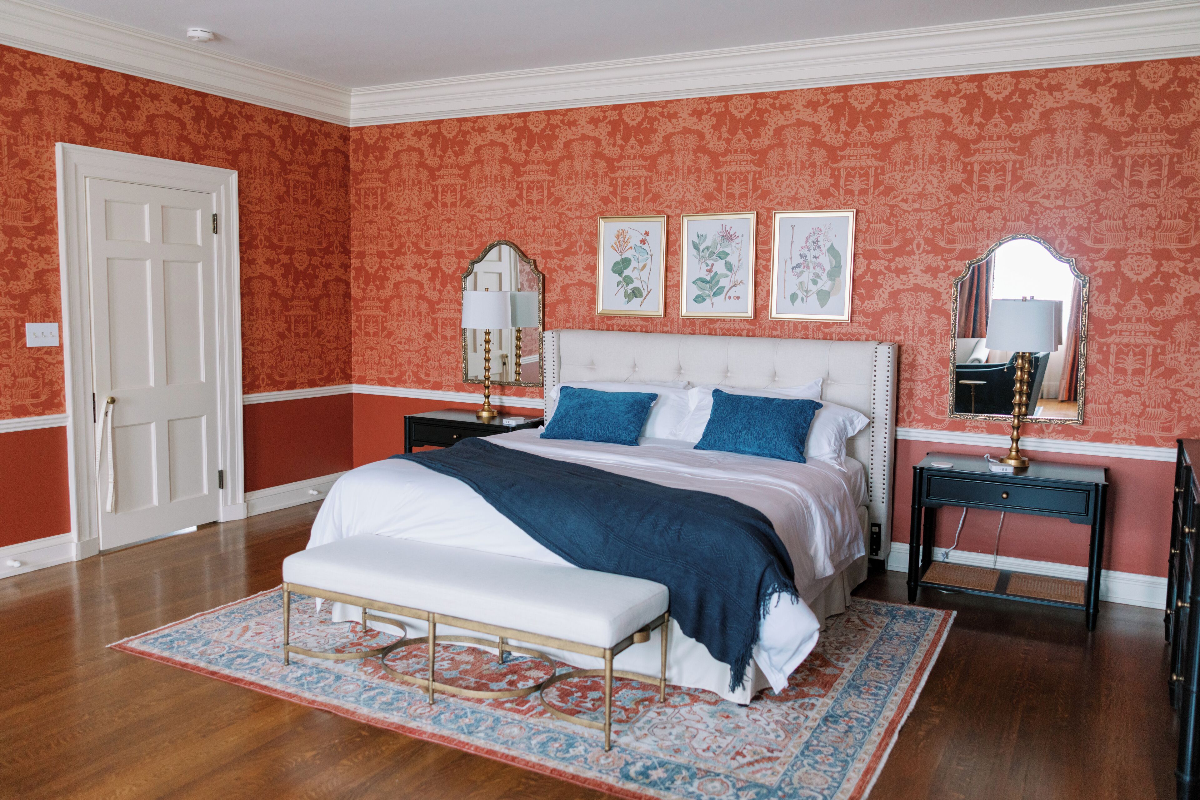 A bedroom with a large bed, a bench, two nightstands, a dresser, and a door.