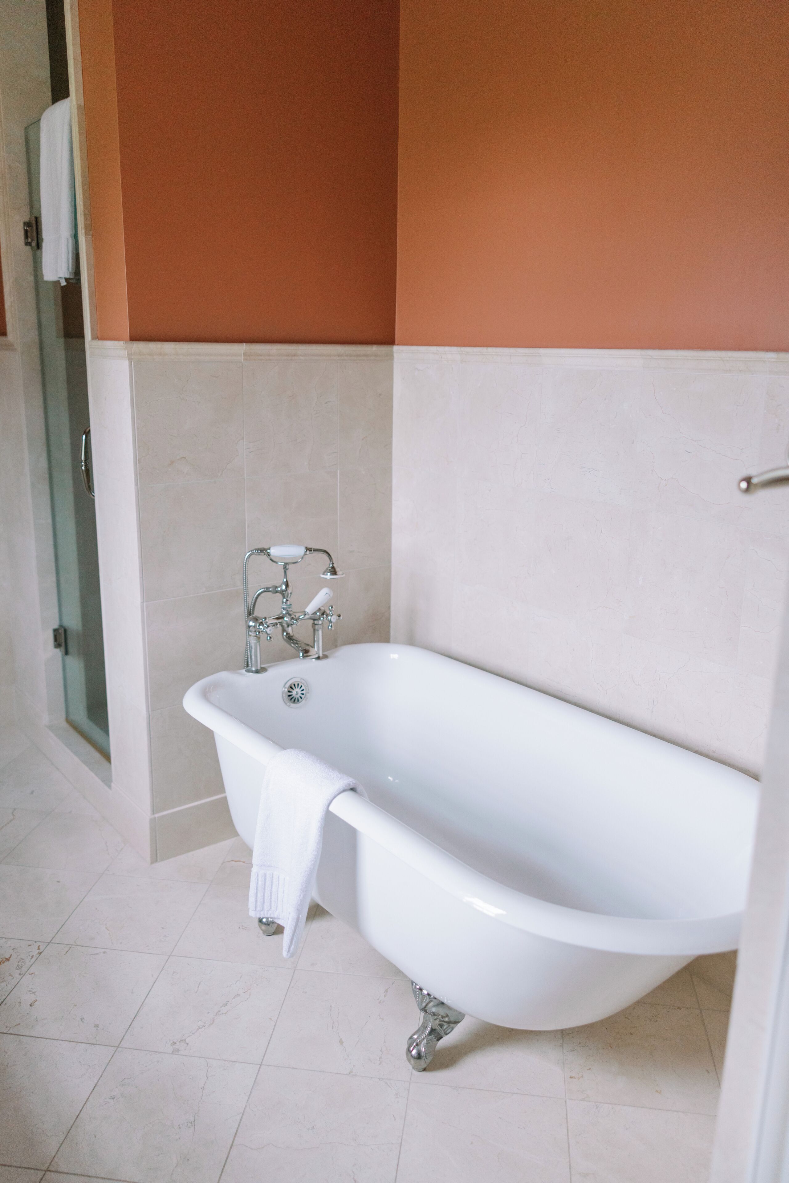 A bathroom with a white bathtub, a glass shower enclosure, and beige tiled walls.