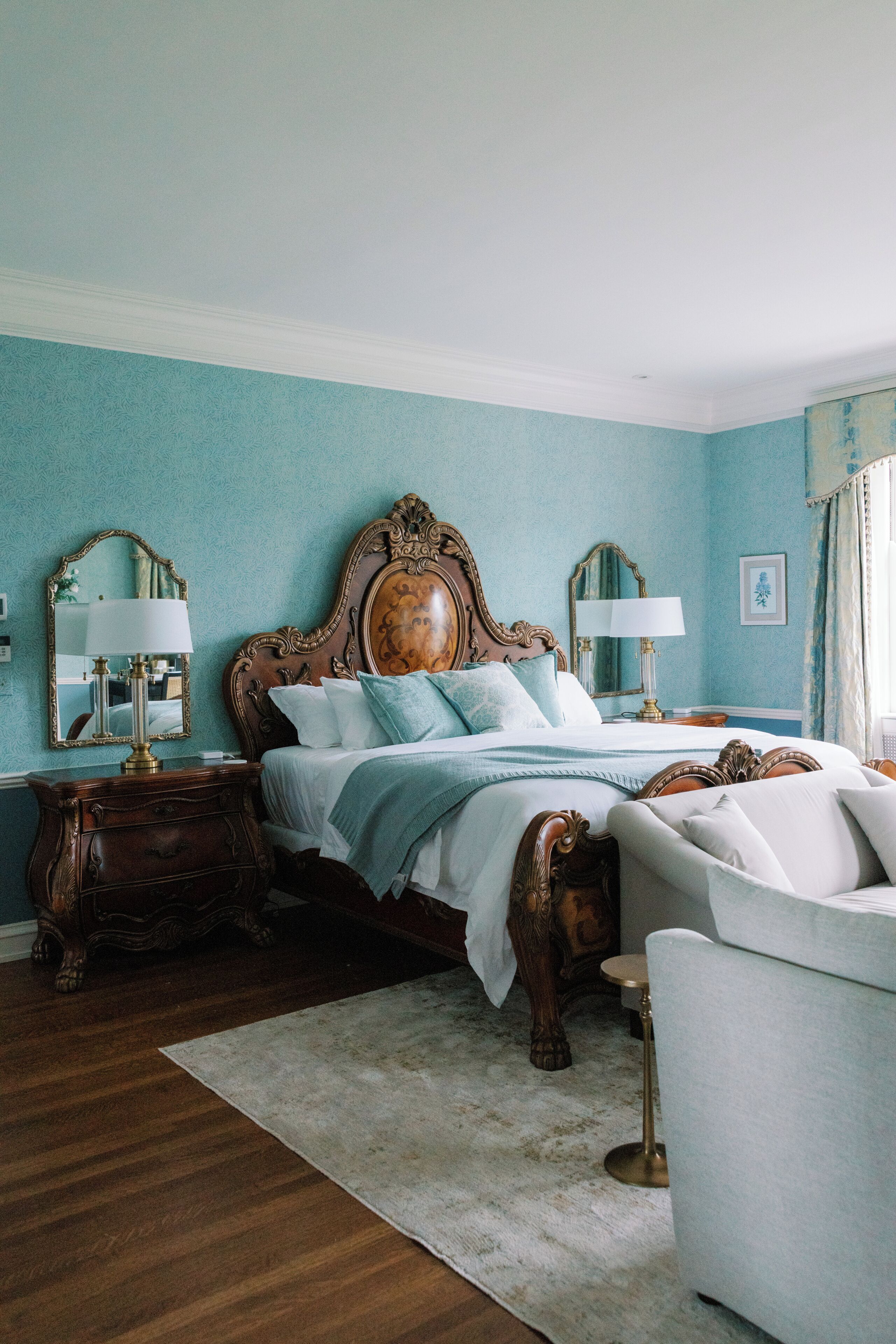 A bedroom with a large bed, two bedside tables, a nightstand, a chair, and a window with curtains.