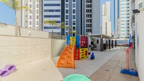 Een kinderspeelplaats met een glijbaan en klimconstructies, omringd door hoogbouw.