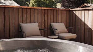 A hot tub with two chairs, surrounded by wooden fencing, with a mountainous landscape in the background. - stieg'nhaus Design Boutique Hotel (Muehlbach Am Hochkoenig)