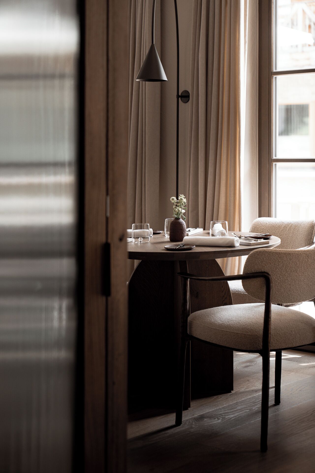 A dining area with a table set for two, a vase of flowers, and a pendant light.
