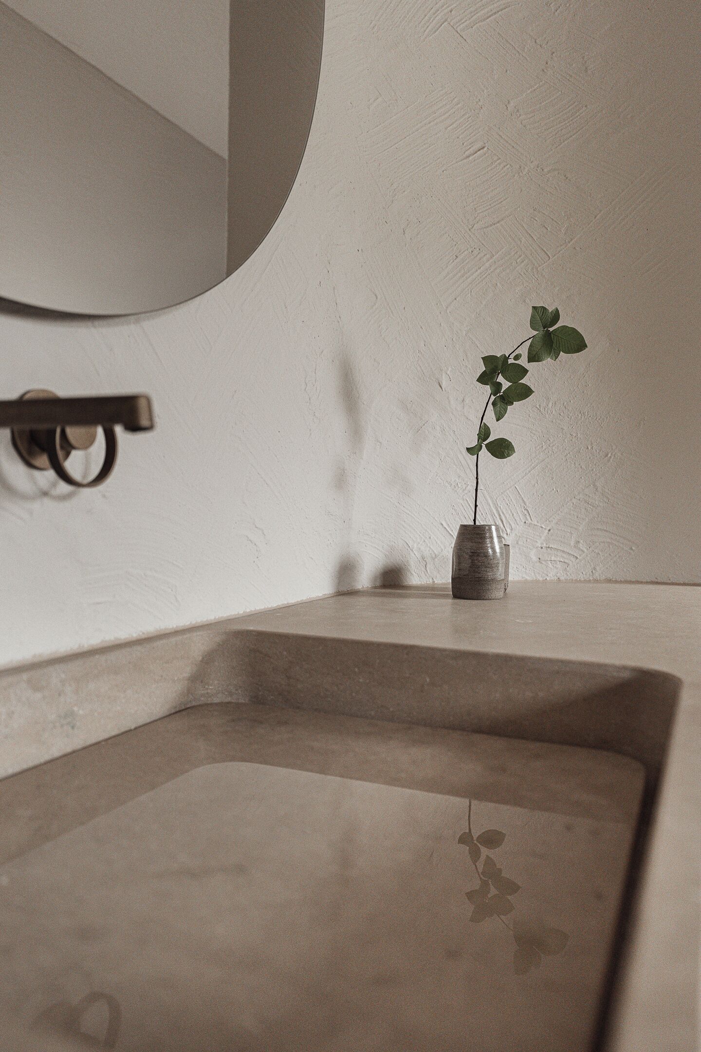 Ein minimalistisches Badezimmer mit großem Spiegel, einer kleinen Vase mit einer einzelnen grünen Pflanze und einem schlichten, klaren Design.