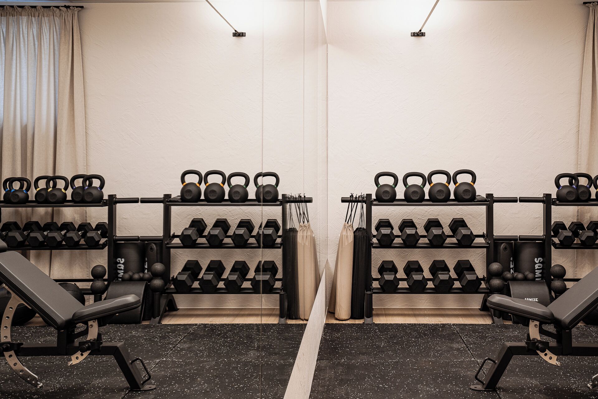 Ein Fitnessstudio mit Spiegelwänden, Gewichtsständern, Bänken und Kettlebells.