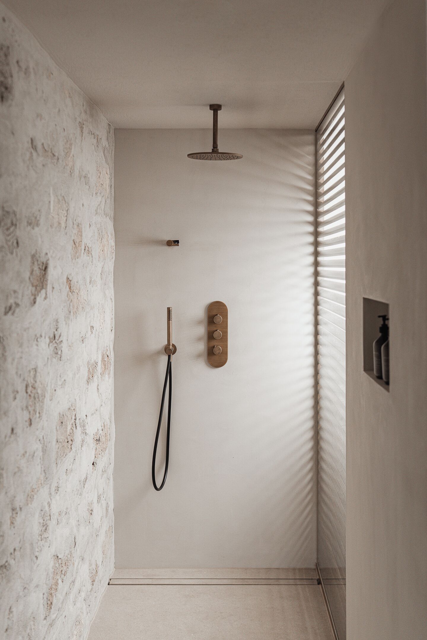 A minimalist bathroom with a textured wall, a showerhead, a handheld shower, and a small shelf with bottles.