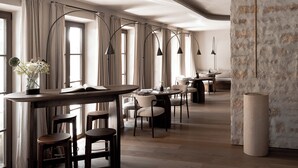 A modern dining area with a long bar, multiple seating options, and large windows with curtains. - stieg'nhaus Design Boutique Hotel (Muehlbach Am Hochkoenig)