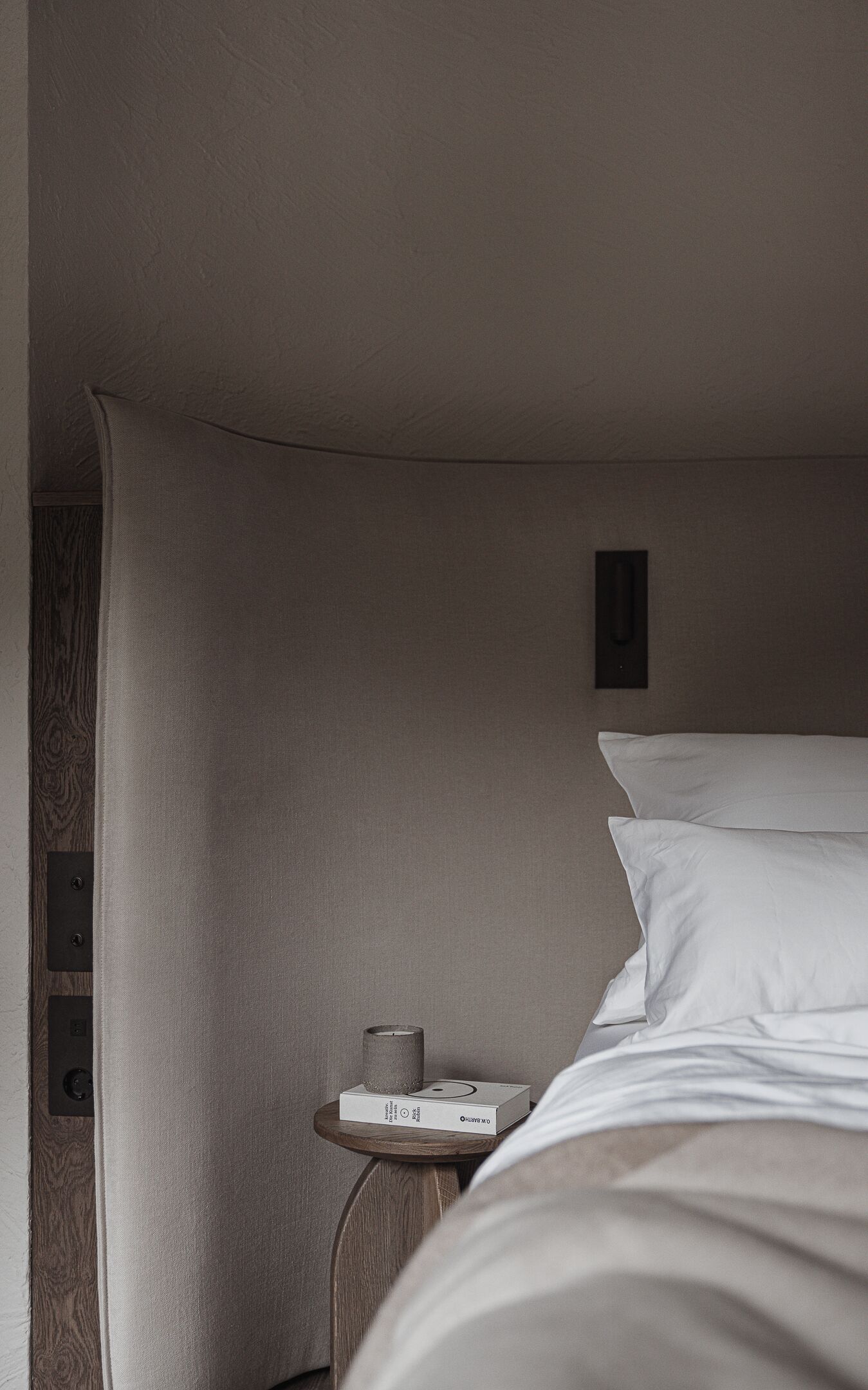 Una habitación de hotel con una cama grande, una mesita de noche con una vela y una pequeña mesita auxiliar de madera.