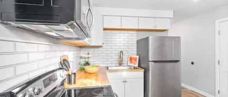 Une cuisine moderne avec un cuisinière noire, des armoires blanches, un réfrigérateur en acier inoxydable et un plan de travail en bois.