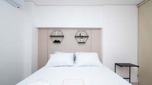 Una habitación de hotel con una cama, dos estantes hexagonales en la pared, una mesita y una puerta.