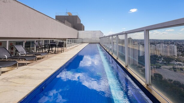 Piscina en la azotea con vista a la ciudad, sillas de descanso y cielo despejado.