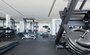 Ein Fitnessraum mit Trainingsgeräten, Laufband und Spiegelwand.