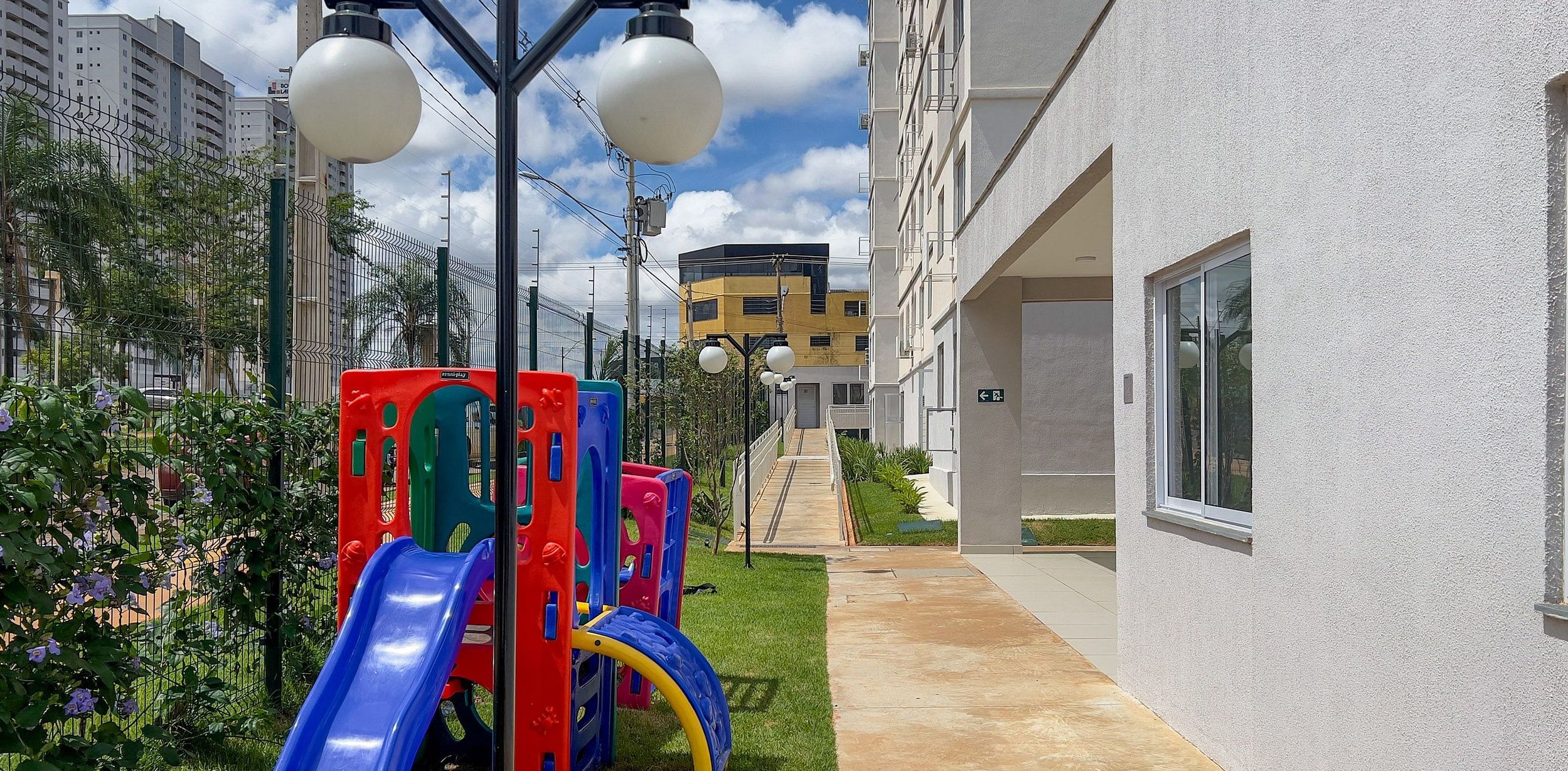 Ein Spielbereich für Kinder mit Rutsche und Klettergerüsten, neben einem Gebäude mit sichtbarem Eingang und einer Treppe, die zu einer oberen Ebene führt.