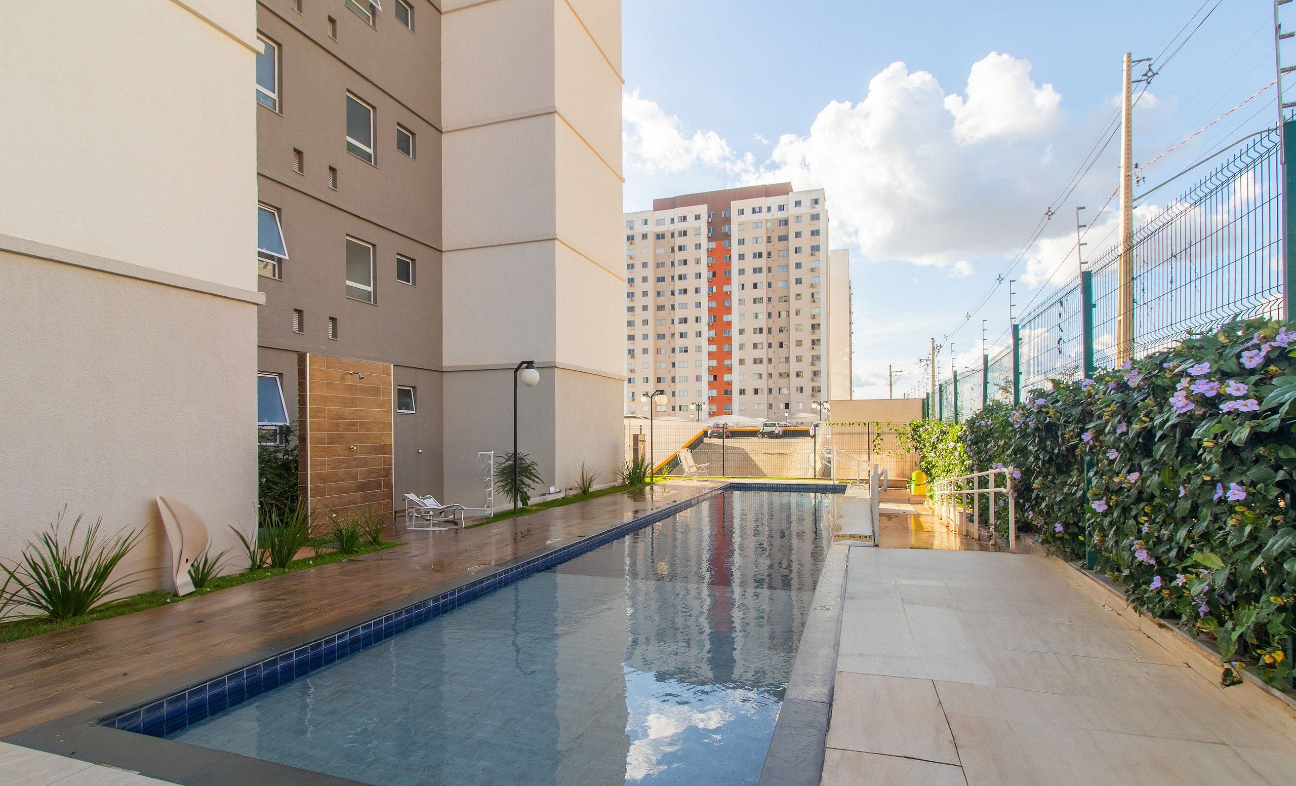 A swimming pool with a tiled deck, a brick wall, and a tall building in the background.