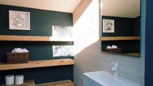 Une salle de bain avec un lavabo blanc, des étagères en bois et un miroir.